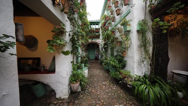 Spain courtyard with whitewashed walls, turquoise doors, cobbles, terracotta pots and hanging planters as the camera tracks into an arched passage with lantern light.