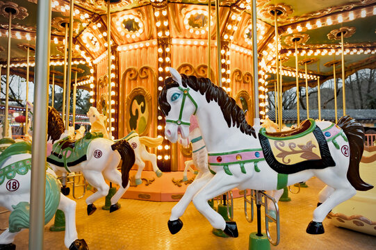 A carousel with brightly colored horses is in motion, set against a backdrop of glowing lights. The central structure is ornate and features a large 'M' emblem. The horses, numbered 1 through 8, are