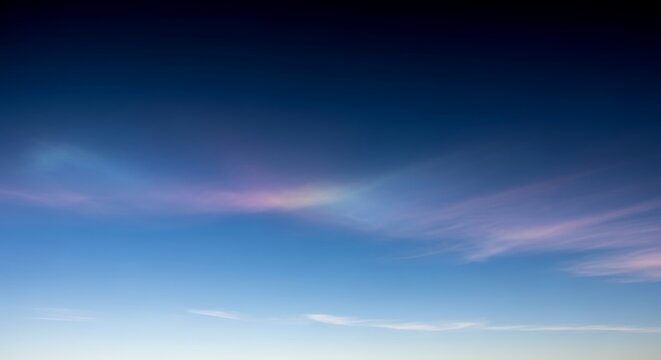 The serene blue sky with a few wispy clouds is transitioning to a peaceful evening atmosphere with hues of pink and purple.