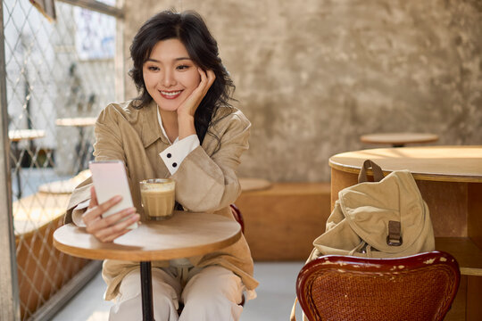Happy young woman snaps pictures of her coffee in a cozy caf��