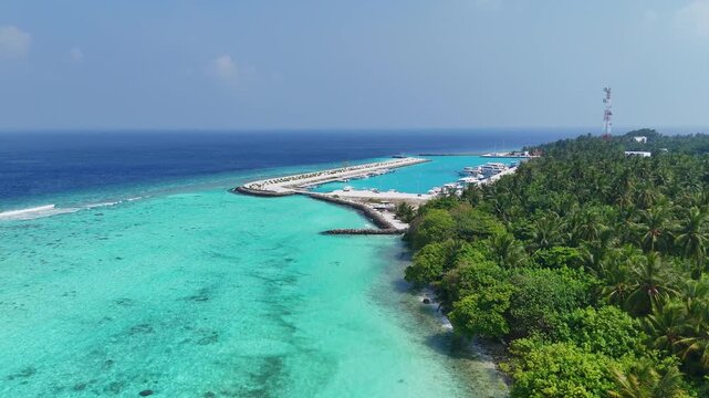 High-angle aerial drone view of the Thoddoo Island coastline, featuring the local boat jetty, lush tropical greenery, and vibrant turquoise water.