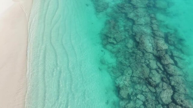High-angle aerial drone view of crystal-clear turquoise ocean water meeting a pristine white sand beach on Ukulhas Island, Maldives; perfect for a tropical background.