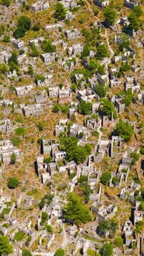 Vertical video. Kayakoy, Turkey. Drone view of abandoned stone architecture in Levissi ghost town on mountain slope, roofless houses and crumbling walls after 1957 earthquake and decades of neglect..