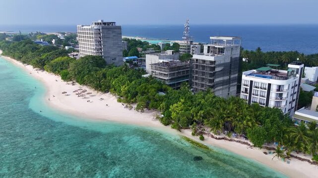 Aerial perspective of growing tourism real estate in Ukulhas, Maldives. Unfinished modern hotel buildings stand near the spectacular turquoise water and white sunset beach.