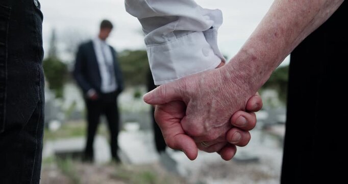 Cemetery, people and holding hands for memorial service, family mourning and compassion for comfort. Sympathy, care and senior woman with son for emotional support, loss and grieving at graveyard
