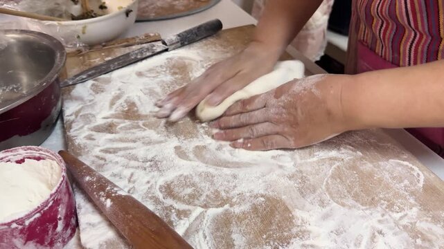 Hands rolling out dough with a wooden rolling pin on a floured board, preparing dumpling wrappers from scratch in a home kitchen for a festive meal in Xi'an, China.