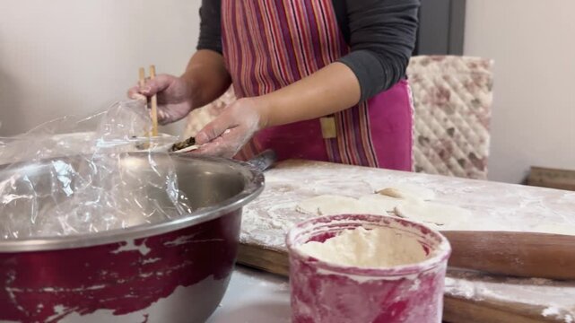 Hands rolling out dough with a wooden rolling pin on a floured board, preparing dumpling wrappers from scratch in a home kitchen for a festive meal in Xi'an, China.