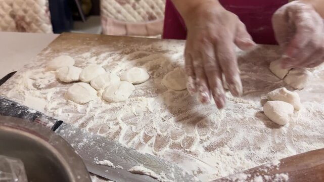 Hands rolling out dough with a wooden rolling pin on a floured board, preparing dumpling wrappers from scratch in a home kitchen for a festive meal in Xi'an, China.