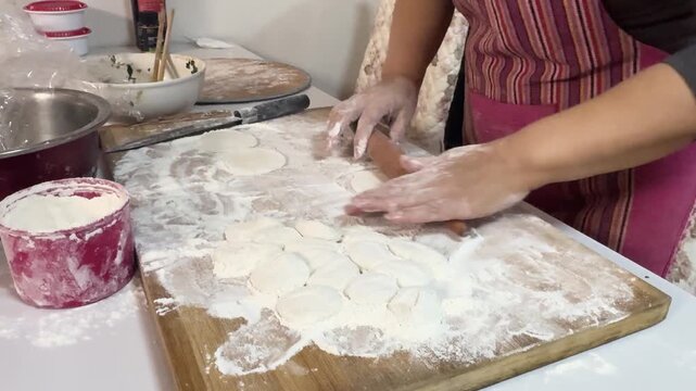 Hands rolling out dough with a wooden rolling pin on a floured board, preparing dumpling wrappers from scratch in a home kitchen for a festive meal in Xi'an, China.