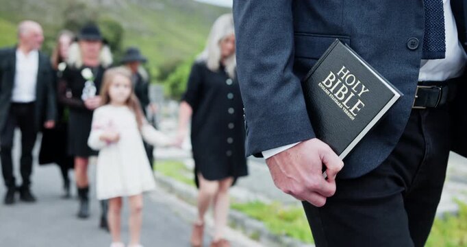 Officiant, family and hand with bible for funeral at cemetery, graveyard or outdoor for farewell. Walking, child or people together for grief, death and respect or support for eulogy, book and pastor