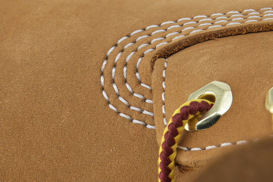 Close-up detail of tan nubuck leather boot with white stitching and braided lace