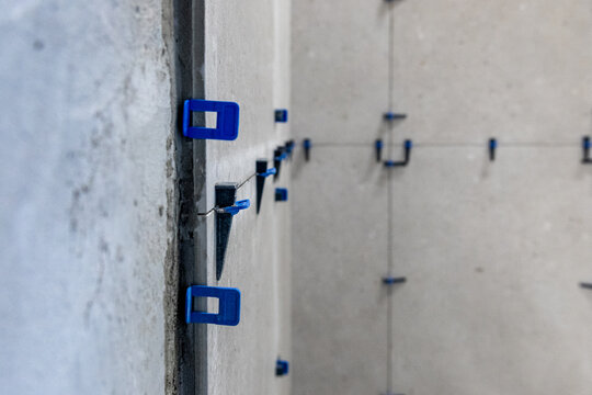 Close-up of blue and black plastic leveling spacers installed between large format tiles on an interior corner.