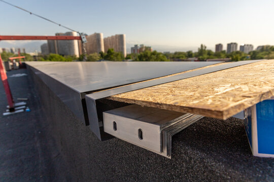 Close-up of metal flashing and OSB board assembly for cornice installation on a flat roof edge during finishing.