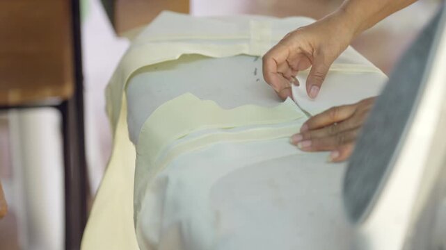 Professional tailor ironing fabric while preparing cloth for garment production in fashion workshop. Clothing preparation process for tailoring, textile craftsmanship and apparel manufacturing.
