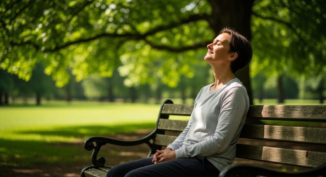 A person sitting on a wooden bench in a green park with eyes closed, enjoying fresh air and sunlight for mental wellness and stress relief