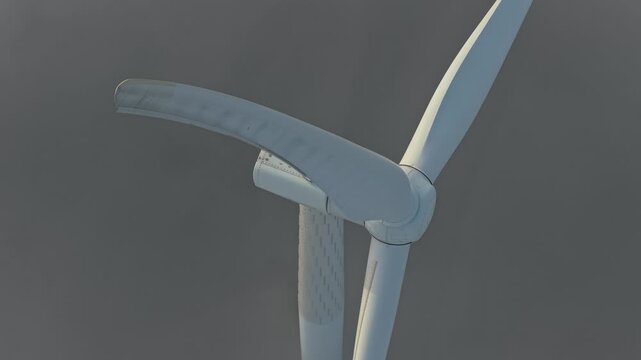 Cinematic aerial view of a large wind turbine slowly rotating. The blades emerge from and disappear into the dense, grey morning fog