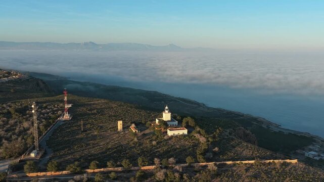 Aerial view of the santa pola lighthouse in spain, perched on a cape overlooking the mediterranean sea covered by a thick layer of fog