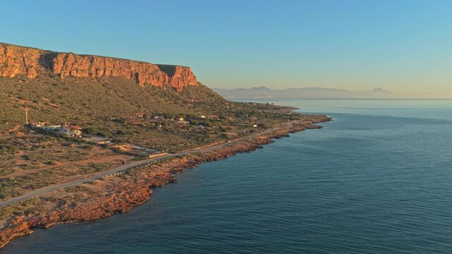 Aerial view of the rocky coastline and cliffs of cape santa pola in spain. Golden hour light hitting the mountains by the mediterranean sea