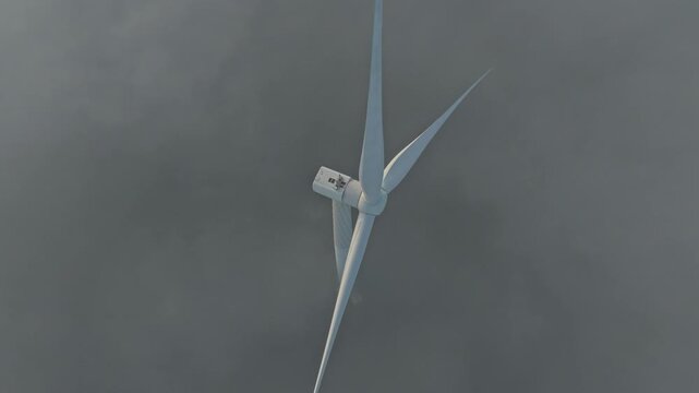 Majestic wind turbine with its large propeller blades rotating to generate clean renewable energy. Thick fog surrounding the wind farm