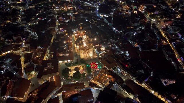 Aerial tilt-up establishing shot of the Santa Prisca temple at night with the giant poinsettia and illuminated streets, north of Guerrero, Mexico