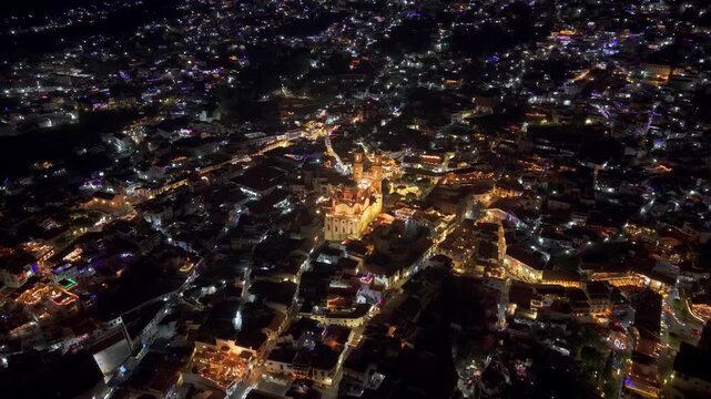 Establishing panoramic aerial view of Taxco de Alarcon at night with illuminated streets connecting it, with the Santa Prisca temple in the center, Guerrero, Mexico