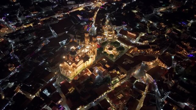Aerial view establishing of the Santa Prisca temple in the magical town of Taxco in Guerrero, at night, with streets illuminated and interconnected with warm light. Colonial architecture, Mexico.