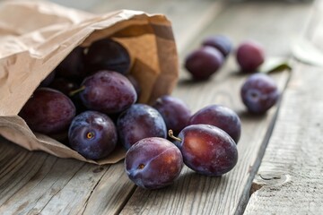 Fototapeta premium Fresh plums spill from a brown paper bag