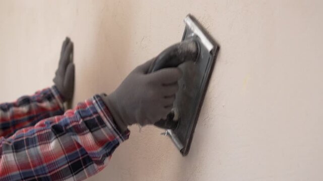 Close up of female builder sanding plastered wall with mesh tool