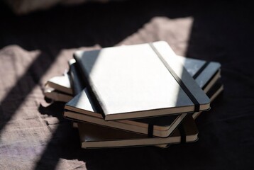 Fototapeta premium A stack of notebooks rests on a textured surface, bathed in sunlight.