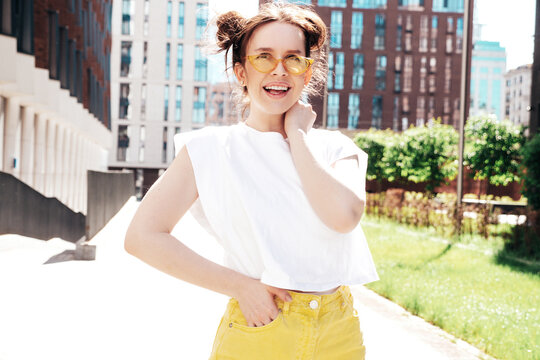 Young beautiful smiling hipster woman in trendy summer yellow jeans clothes. Carefree teen model posing in the street at sunset. Positive female outdoors. Cheerful and happy. In sunglasses