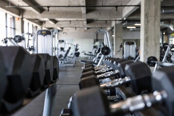Fototapeta premium A gym interior with weight machines and dumbbells. People are exercising, likely working out. It’s a modern fitness center with concrete ceilings and flooring.