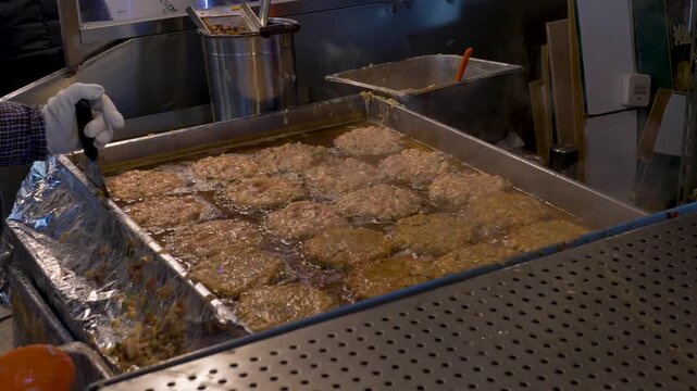 Slow motion view of meat bindaetteok patties cooking in oil on stove top burner while vendors wearing gloves hold utensils at Gwangjang night street market stalls in Seoul city South Korean cuisine