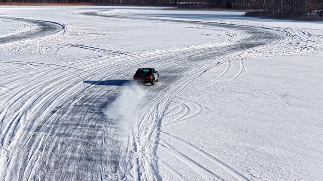 Aerial slow motion shot following a drifting car carving curved patterns in a wide white snow field.