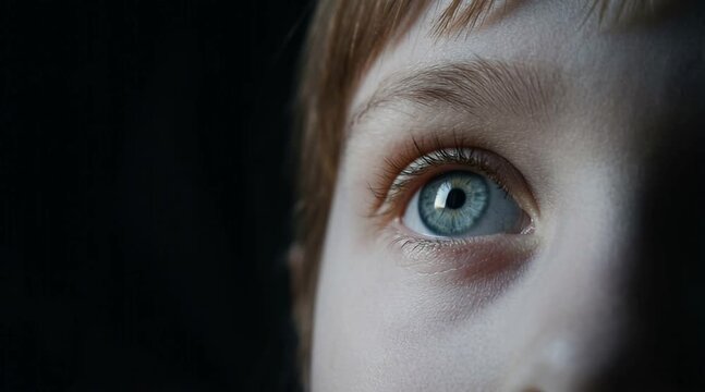 extreme macro close up of beautiful blue green eye of a child with long lashes against dark dramatic background