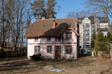 Fototapeta premium Historic pink house with a tiled roof surrounded by trees and modern buildings in Svetlogorsk Kaliningrad, showcasing architectural contrast and urban landscape