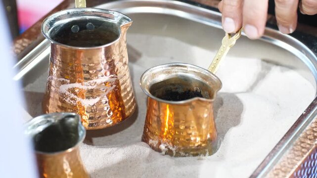 Close up of copper pots placed in hot sand for traditional turkish coffee brewing. Authentic oriental technique of making strong caffeine drink in a metal cezve or ibrik.