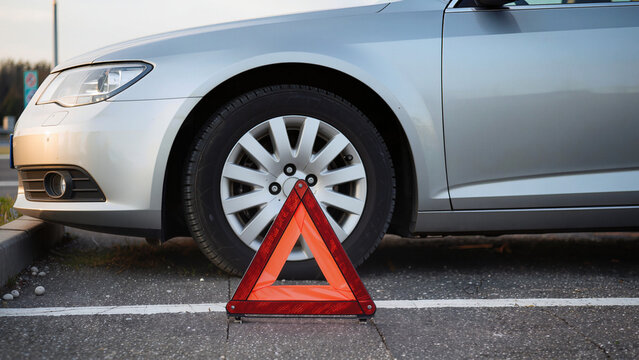 car on the road, The vehicle appears to have a breakdown, Emergency signaling is visible in the foreground, A warning sign alerts oncoming traffic, The driver is experiencing technical issues