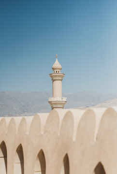 Minaret of islamic mosque towers above crenelated walls, Oman