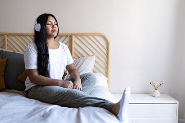 Young latina woman relaxing on bed listening to music with headphones