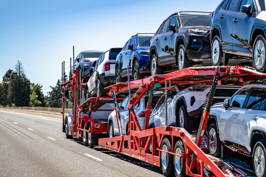 Car hauler white big rig semi truck transporting cars and crossovers on two level modular semi trailer running on the wide highway road