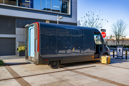 Dark gray electrical cargo mini van with open door making delivery standing on the urban city street
