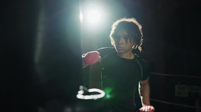 Motivated box fighter training alone, striking punch bag by arms, portrait. Professional sportsman practicing in gym, preparing to competition and championship, sportive hobby and self-defense class