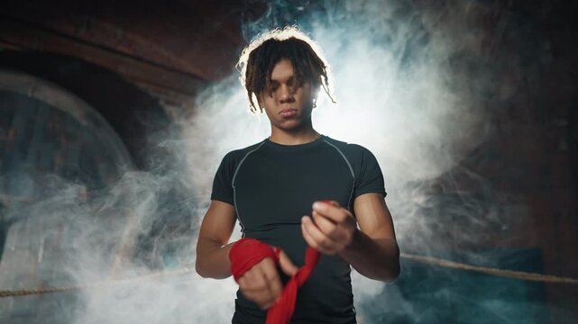 Young adult athletic man preparing to box fight, wrapping hands by elastic tape . Portrait of professional fighter in fight club, masculinity and aggression, do sport for hobby and healthy lifestyle