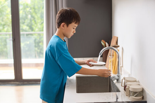 A boy does the dishes in the kitchen