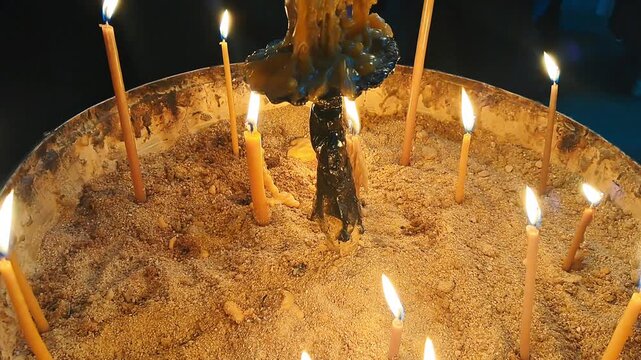 Candles burning in a circular holder with sand, wax drips visible around