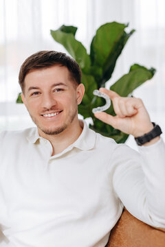 Smiling man holding a clear dental aligner showing orthodontic treatment and confident healthy smile
