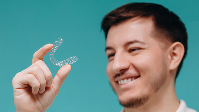 Smiling young man holding a clear aligner for dental orthodontic treatment and cosmetic teeth care