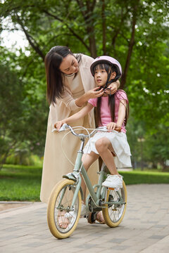 Mother helps her daughter put on her protectors to get ready for a bike ride