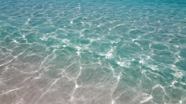 Clear turquoise water surface with gentle ripples and reflections, showcasing the gradual transition from shallow to deeper areas in a serene coastal environment