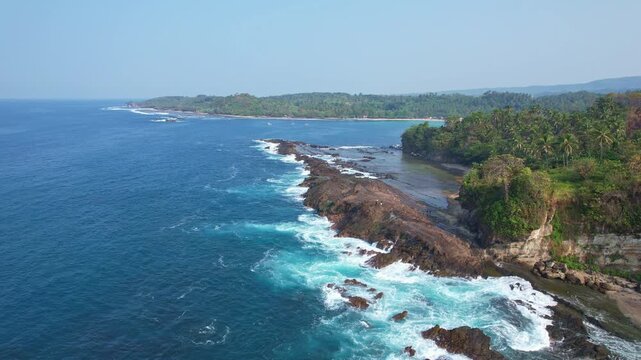 Aerial drone footage of Karang Taraje rock formation, creating waterfalls, in Legon Pari beach, Lebak Regency, Banten, Java island, Indonesia, with forests around, beautiful clear blue sea 